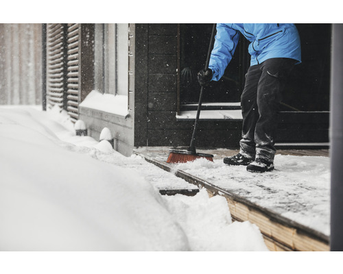 Persoană care mătură zăpada cu o mătură în fața intrării casei