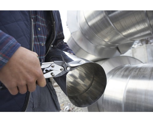 Un bărbat taie o țeavă metalică cu foarfece de tablă.