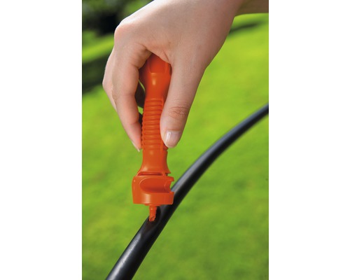 O mână folosește o unealtă pentru a perfora un furtun de irigare.