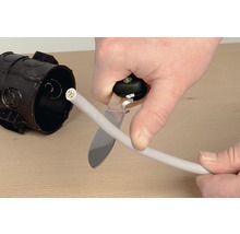 Electrician taie un cablu cu un cuțit de cablu lângă o cutie de joncțiune