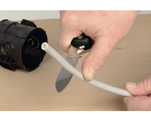 Electrician taie un cablu cu un cuțit de cablu lângă o cutie de joncțiune