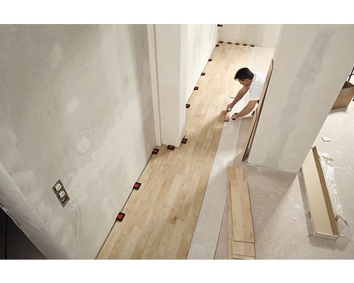 Un bărbat instalează podea din lemn într-o cameră cu ajutoare de nivelare.