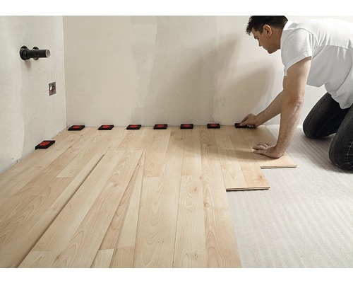 Bărbat care instalează podea laminată cu distanțiere pe perete