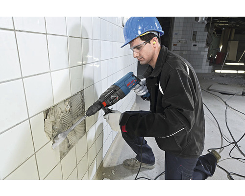 Muncitor cu ciocan rotopercutor care îndepărtează plăcile de pe un perete.