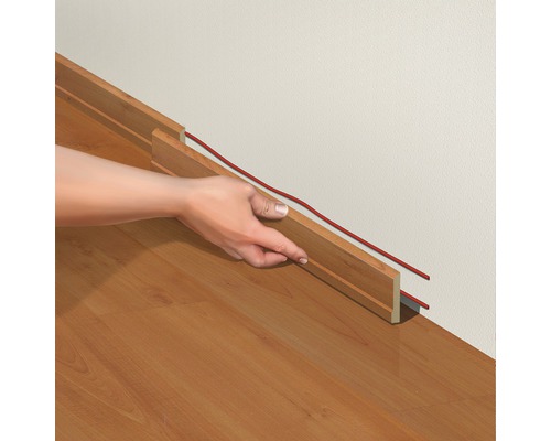 O persoană instalează o plintă cu canal de cablu pe un perete