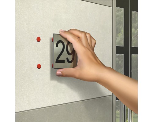 O mână fixează un număr de casă cu numărul 29 pe perete.