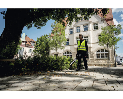 Bărbat cu suflantă de frunze curăță trotuarul din fața clădirii