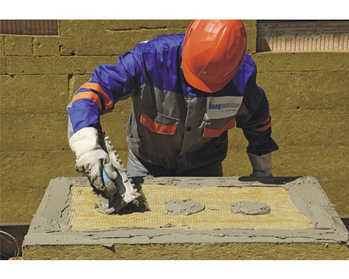 Un muncitor fixează o placă izolatoare cu mortar pe un perete.