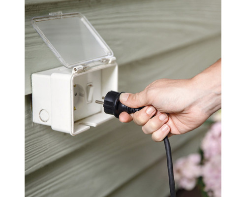 O persoană introduce o priză într-o priză exterioară impermeabilă.