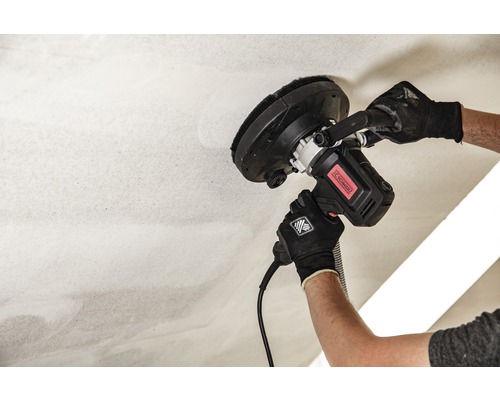 Un bărbat șlefuiește un tavan cu o mașină de șlefuit tavanul.