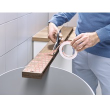 O persoană taie bandă adezivă dublă cu foarfeca pentru a o lipi pe o scândură de lemn.