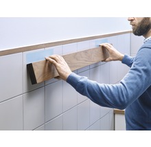 O persoană fixează o poliță de lemn pe un perete faianțat.