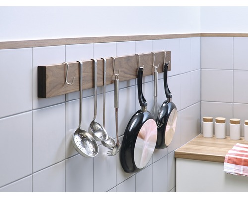 Ustensile de bucătărie și tigăi atârnate de o bară de bucătărie pe perete.