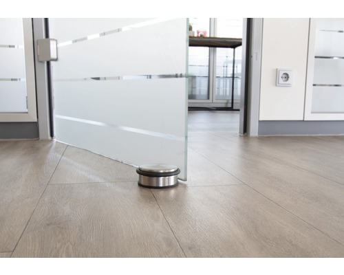 Opriitor de ușă din oțel inoxidabil pe podea de lemn în fața unei uși de sticlă