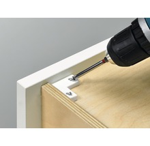 O șurubelniță cu acumulator fixează un conector unghiular pe o piesă de mobilier.