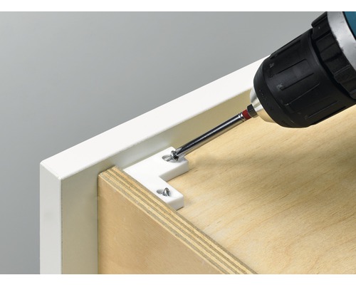 O șurubelniță cu acumulator fixează un conector unghiular pe o piesă de mobilier.