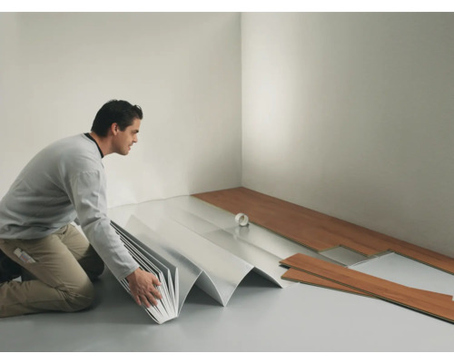 Un bărbat montează podea laminată într-o cameră cu izolație fonică.