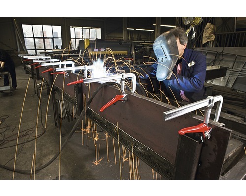 Un bărbat sudează metal cu o menghină într-un atelier.