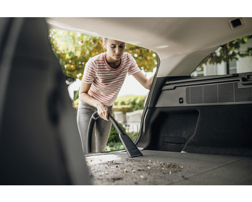 Femeie aspirând portbagajul unei mașini cu un aspirator