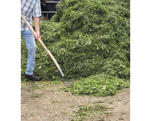 Persoană cu furcă de gunoi și o grămadă mare de iarbă