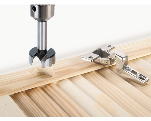 Burghiu Forstner găurește o gaură lângă balamaua mobilei într-o scândură de lemn