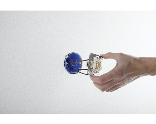 O mână montează un întrerupător într-o cutie de perete.