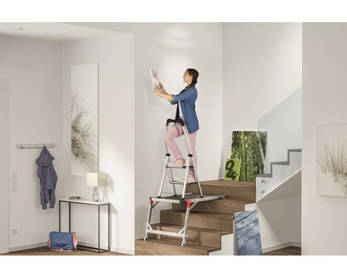 Femeie pe o scară cu platformă într-o scară luminoasă, agățând un tablou