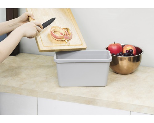 "O persoană aruncă coji de mere de pe un tocător de lemn într-un coș de gunoi