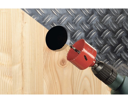 Freza carotieră găurește o gaură în lemn în fața unei plăci metalice