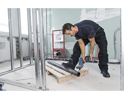 Un bărbat taie o țeavă cu un ferăstrău electric într-o baie în construcție.