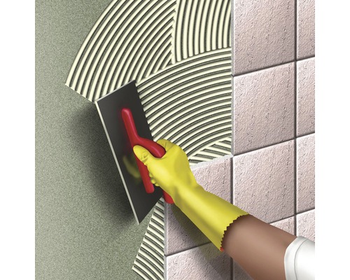 O persoană aplică adeziv pentru plăci ceramice cu o mistrie