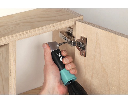 O persoană fixează o balama de mobilier pe un dulap din lemn cu o șurubelniță unghiulară.