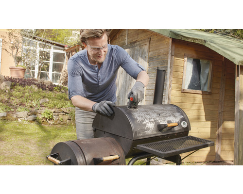 Un bărbat curăță un grătar cu o mașină de șlefuit în grădină.