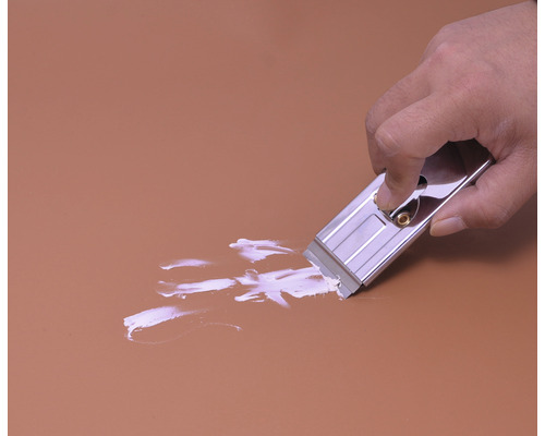 O mână folosește un răzuitor de sticlă pentru a îndepărta vopseaua de pe o suprafață.