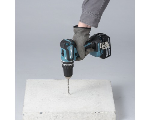 O mână cu mănușă forează o gaură într-un bloc de beton cu o șurubelniță de găurit cu acumulator.