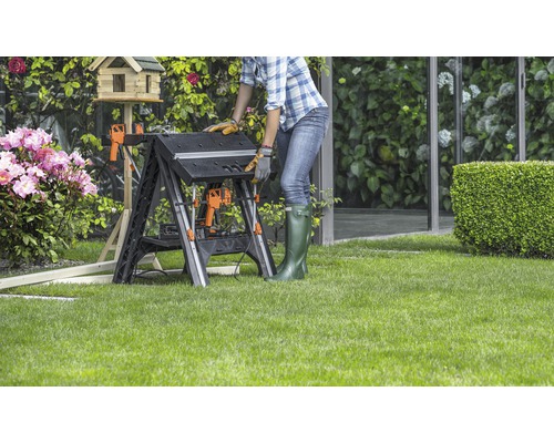 Femeie lucrând la un banc de lucru pliabil în grădină.