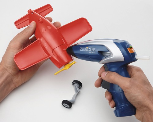 Persoană care lipește un avion roșu de jucărie cu un pistol de lipit