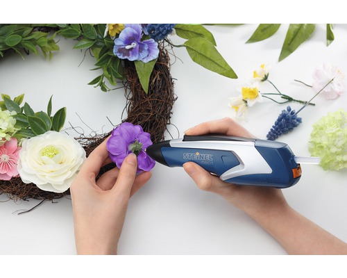 O persoană fixează o floare pe o coroană cu un pistol de lipit cu topire.