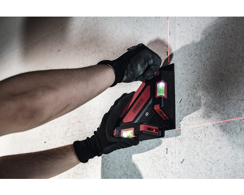 O persoană fixează o nivela laser cu linii încrucișate pe un perete.