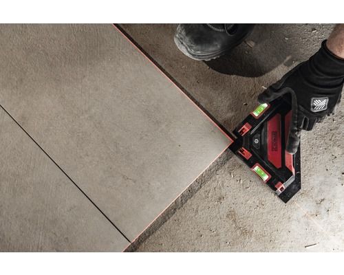 Un bărbat montează gresie cu un echer laser.