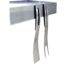 Accesorii pentru grătar, cum ar fi spatulă și furculiță metalică, agățate de o masă pentru grătar.