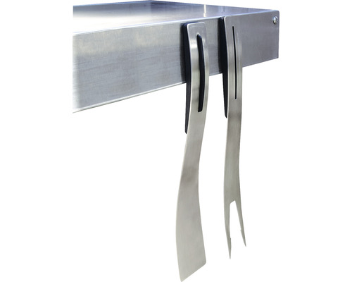 Accesorii pentru grătar, cum ar fi spatulă și furculiță metalică, agățate de o masă pentru grătar.