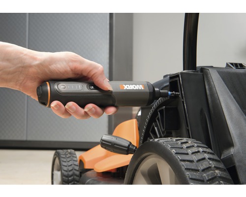 O mână ține o șurubelniță cu acumulator care este utilizată pe o mașină de tuns iarba.