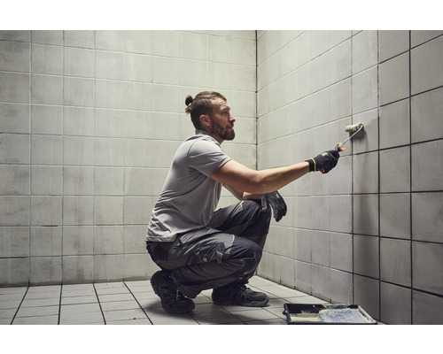 Un bărbat vopsește faianța cu trafaletul într-o cameră.