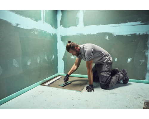 Artizan care lucrează suprafața podelei în baie cu o mistrie pentru lucrări de renovare