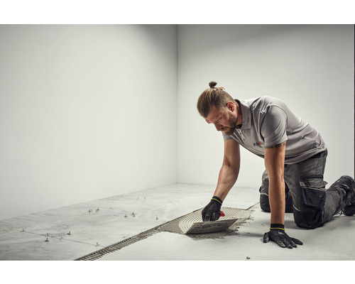 Faiantar aplicând adeziv pe plăci cu o mistrie.