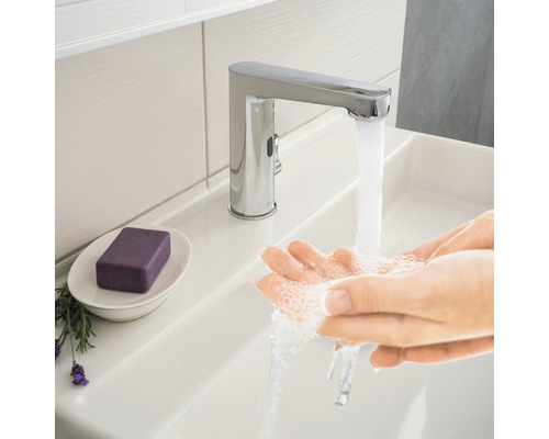 Persoană care se spală pe mâini sub un robinet cromat în chiuveta de baie.