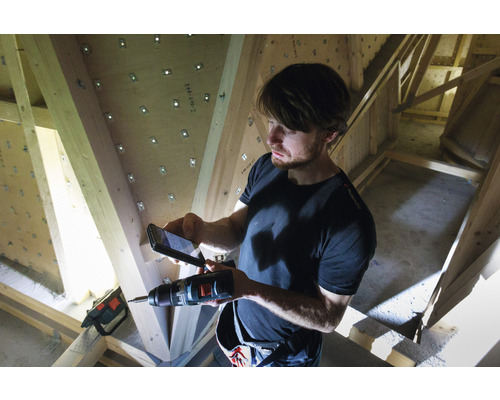 Un bărbat fotografiază cu un telefon mobil o mașină de găurit în fața unei ferme de lemn