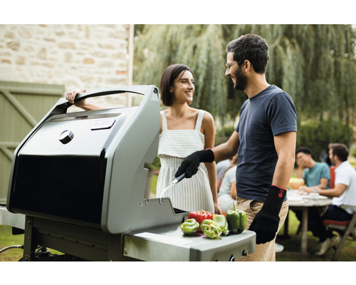 Un cuplu face grătar cu un grătar pe gaz în grădină. Pe grătar sunt ardei grași.