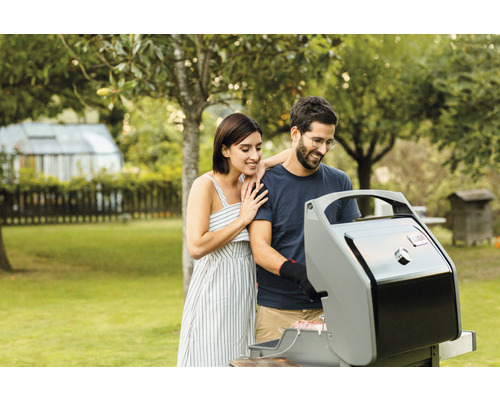 Un cuplu face grătar într-o grădină cu un grătar pe gaz